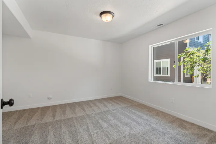 Spacious room featuring neutral carpeting, white walls, a large window, white trim, and a flush mount ceiling light fixture