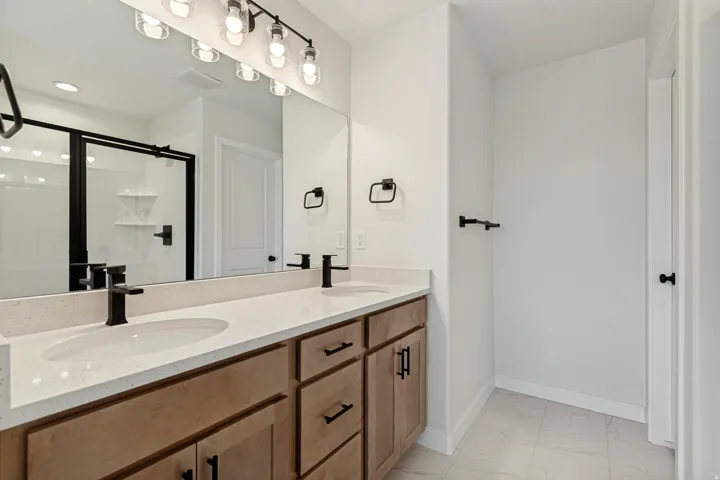 Dual sink vanity with light wood-finish cabinetry, light-toned countertops, and matte black fixtures