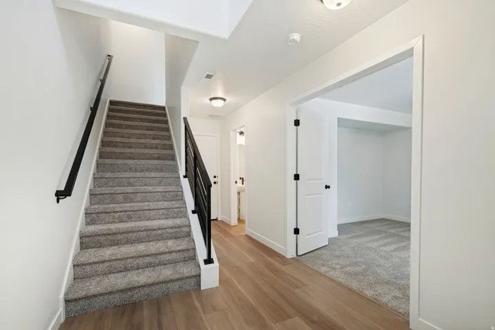 Carpeted staircase with black metal railing, wood-finish flooring, white trim, and recessed lighting