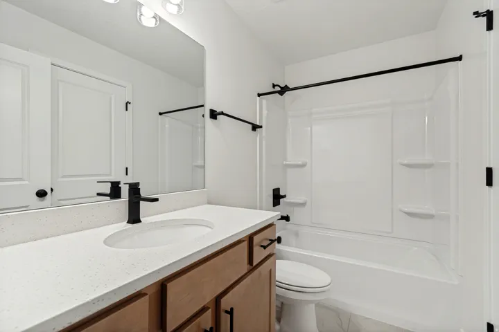 Full bathroom featuring a single vanity with a white countertop and undermount sink, a matte black faucet, and wood-finish cabinetry