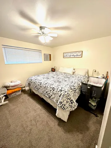 Carpeted room featuring a window with blinds, ceiling fan with integrated lighting, and a wall-mounted vent