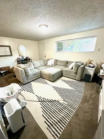 Living area featuring a horizontal window with blinds, a white door, and overhead flush-mount lighting