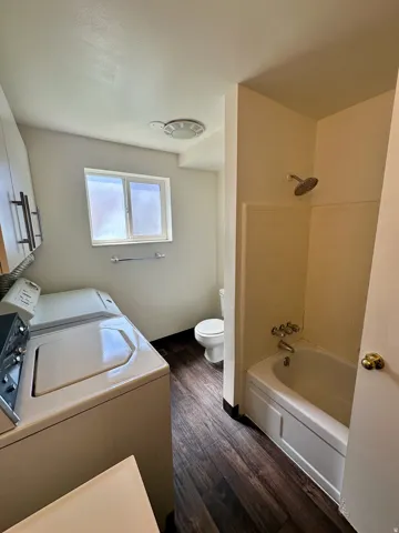 Full bathroom featuring a shower-over-tub combination, a toilet, and wood-finish flooring