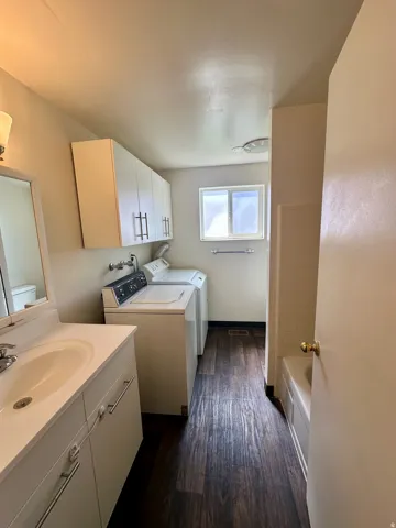 Full bathroom featuring a white vanity with integrated sink, white upper cabinetry, and wood-finish flooring