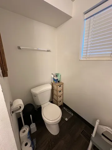 Powder room featuring a white toilet, dark wood-finish flooring, and a window with white blinds