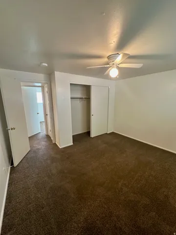 Spacious room featuring brown carpet flooring, white walls, and a ceiling fan with integrated lighting