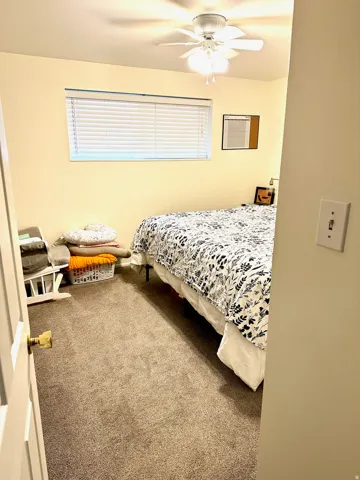 Carpeted interior space featuring a ceiling fan with integrated lighting, a window with horizontal blinds, and light-toned walls
