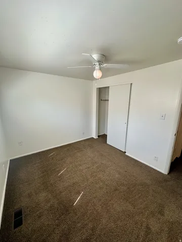 Carpeted room featuring a ceiling fan with integrated lighting, white walls, and a closet with bi-fold doors