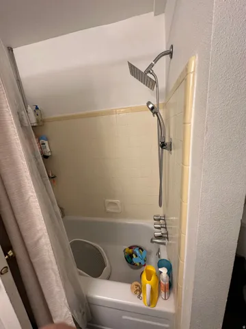 White bathtub with integrated shower system featuring both a rainfall showerhead and a handheld sprayer