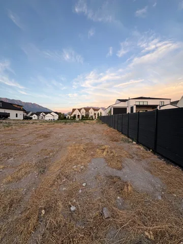 Expansive lot with varied terrain and dry vegetation, bordered by a dark, horizontal slatted fence