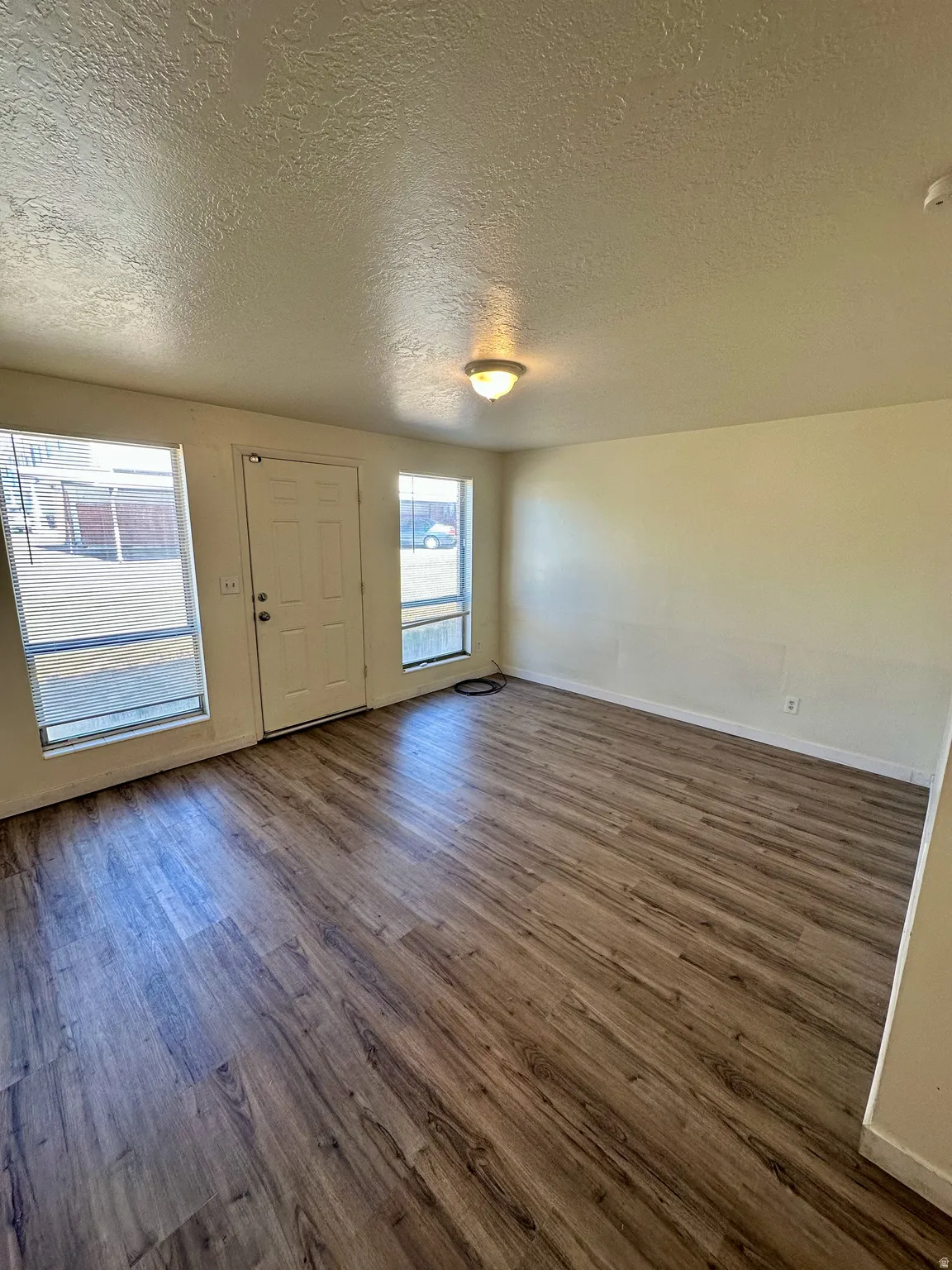 Spacious room featuring wood-finish flooring, light-toned walls, and a white entry door
