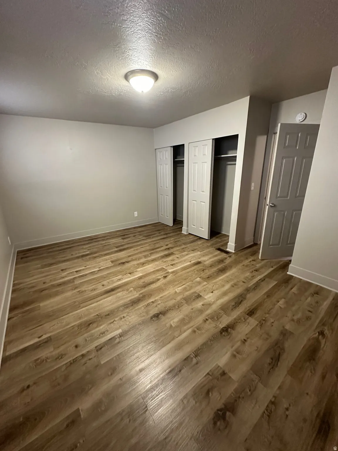 Spacious room featuring wood-finish flooring, two bi-fold closet doors with interior shelving, a flush-mount ceiling light, and a white interior door