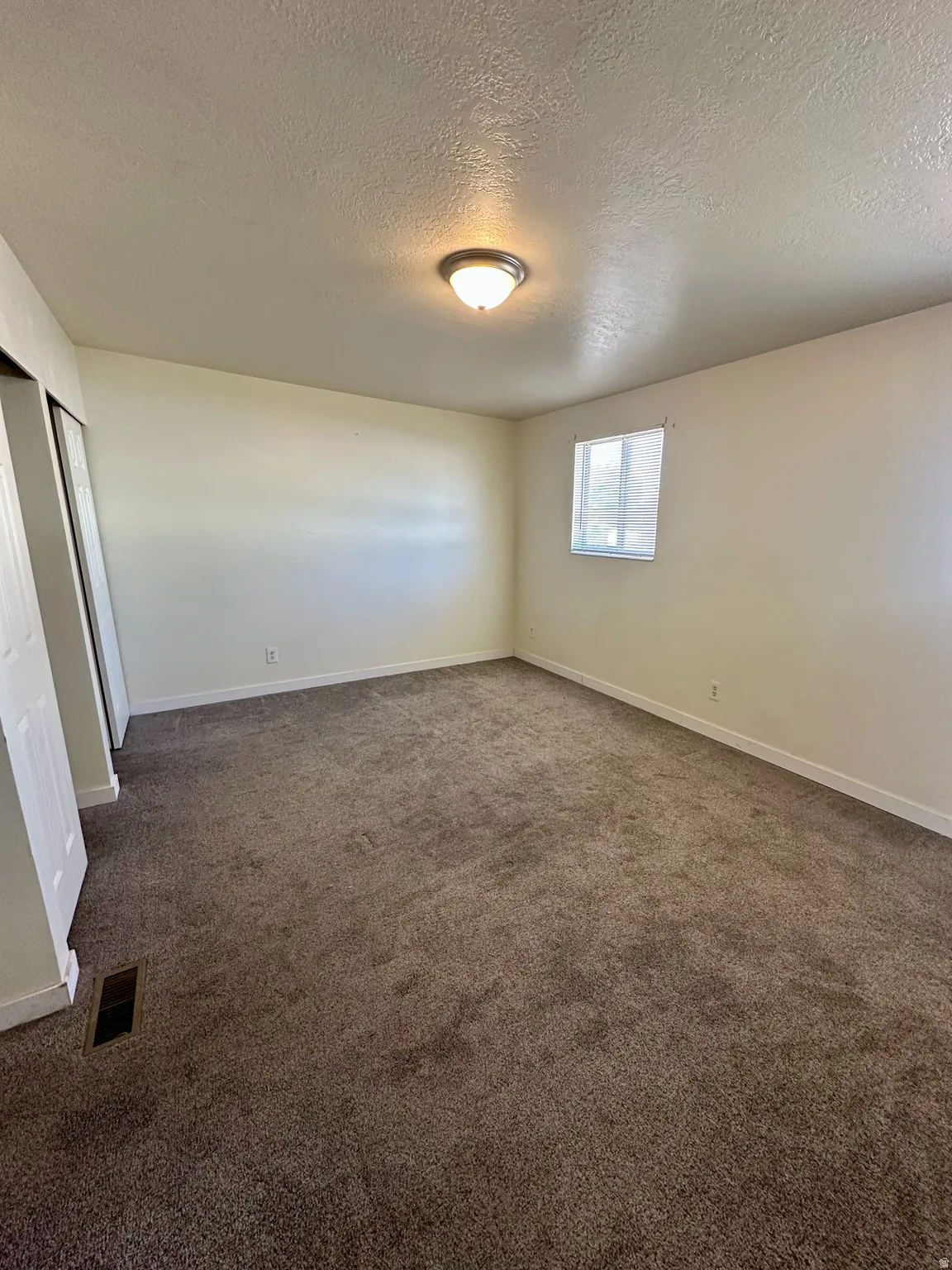 Carpeted room with a single window featuring horizontal blinds