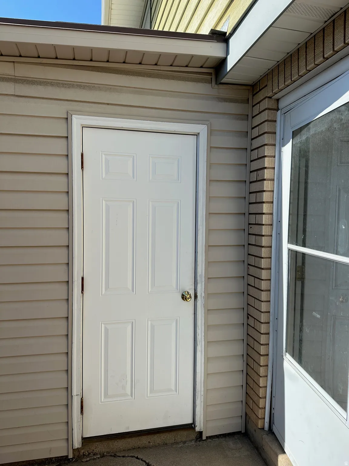 Six-panel white door with a brass-finish knob, set within beige horizontal siding
