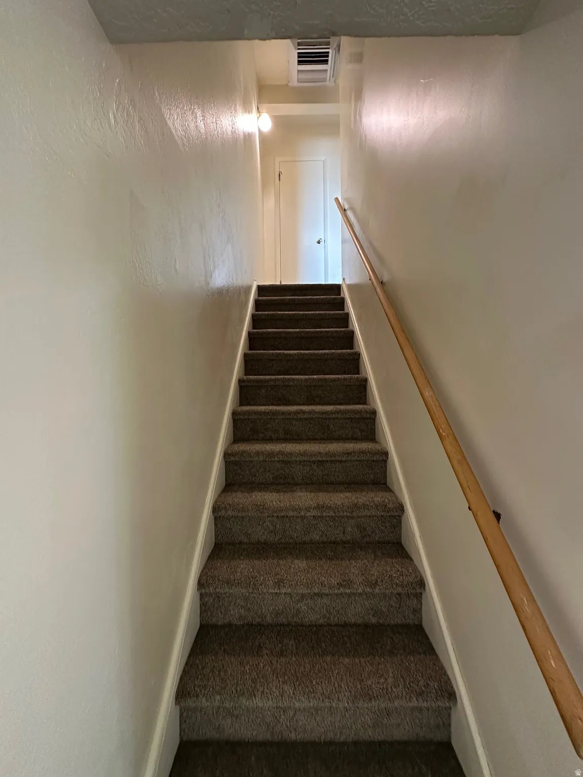 Carpeted staircase featuring a light-toned wood handrail, white baseboards, and overhead lighting