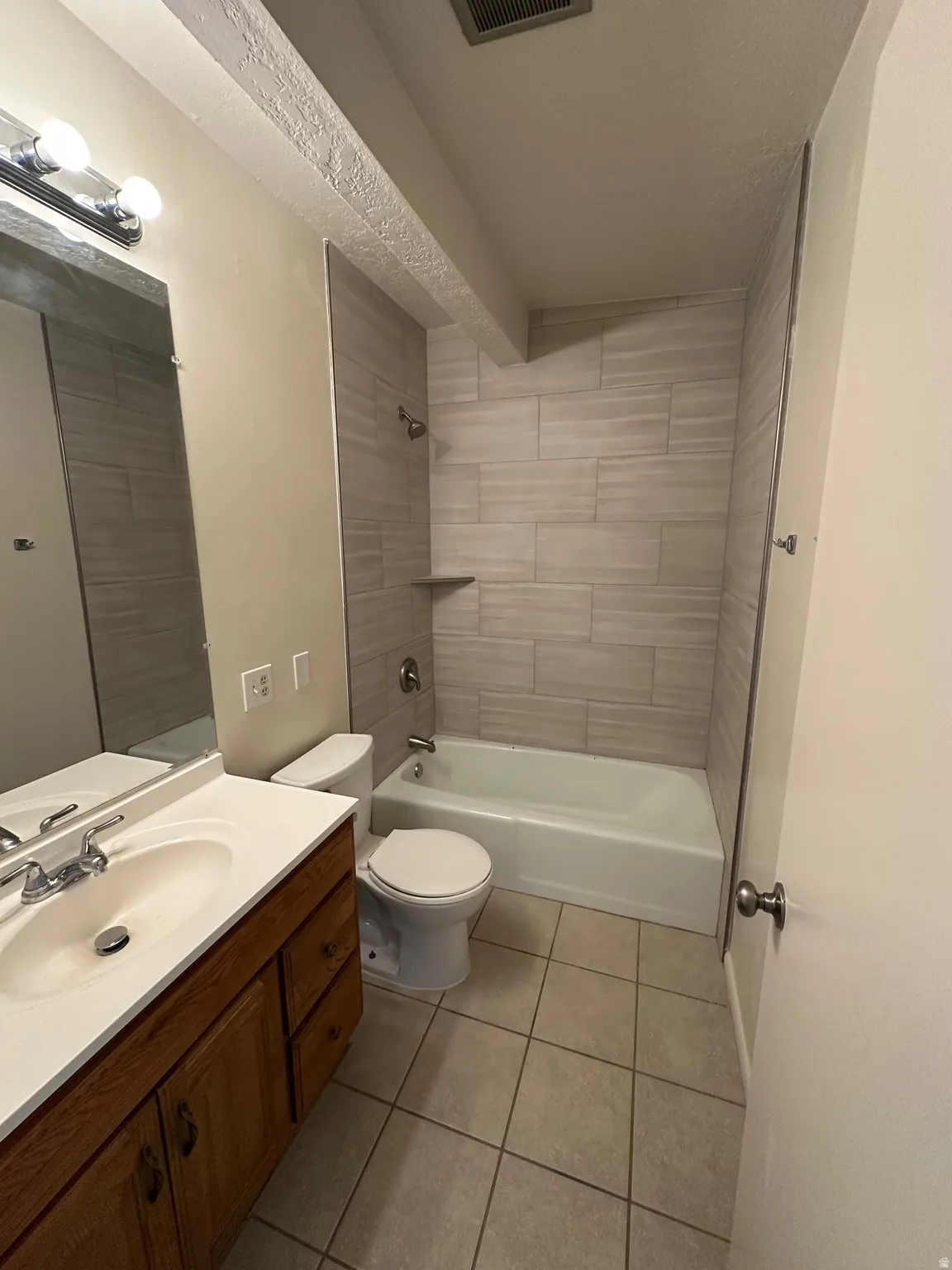 Bathroom featuring a wood-finish vanity with a white countertop and integrated sink, a commode, and a tub with tiled surround