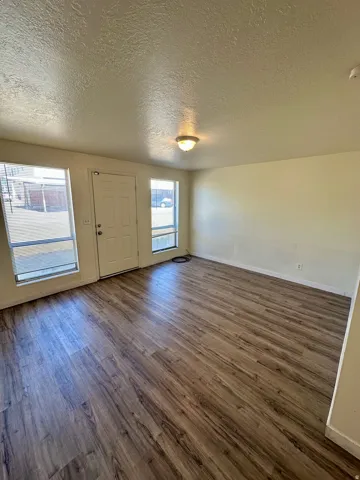 Spacious room featuring wood-finish flooring, light-toned walls, and a white entry door