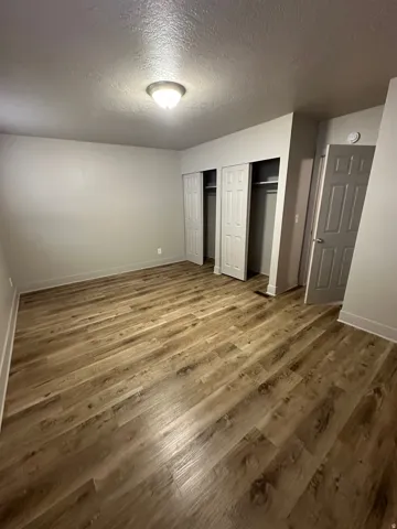 Spacious room featuring wood-finish flooring, two bi-fold closet doors with interior shelving, a flush-mount ceiling light, and a white interior door