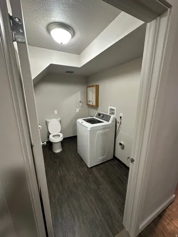 Practical utility room featuring wood-finish flooring, a toilet, a laundry hookup, and a wall-mounted medicine cabinet