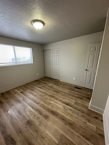 Spacious room featuring wood-finish flooring, a contemporary ceiling light fixture, a window with blinds, and white bi-fold closet doors