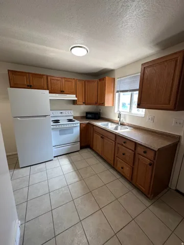 Corner kitchen featuring wood cabinetry, laminate countertops, a double basin sink, and tile flooring