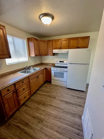 Functional kitchen featuring wood-finish cabinetry, a double basin stainless steel sink, and a full suite of white appliances