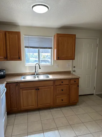 Kitchen featuring wood cabinetry, a double basin stainless steel sink with a dark-finish faucet, and a neutral countertop