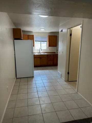 Kitchen with tile flooring featuring wood cabinetry, a white refrigerator, and a stainless steel sink with a window above