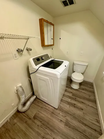 Dedicated laundry area featuring wood-finish flooring, a wall-mounted storage cabinet, and an overhead wire shelf