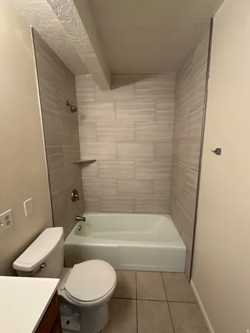 Bathroom featuring a tiled shower surround with a built-in shelf, bathtub, and toilet