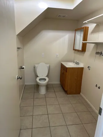 Full bathroom featuring a white toilet, wood-finish vanity with an integrated sink, and a mirrored medicine cabinet