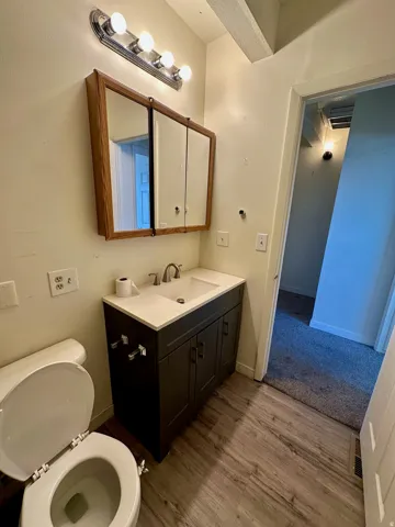 Bathroom featuring a dark wood-finish vanity with a white countertop and integrated sink, a chrome faucet, and a tri-fold medicine cabinet with a wood-finish frame