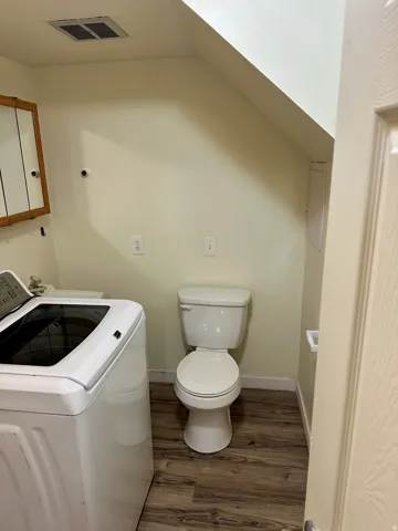 Compact utility space featuring wood-finish flooring and a white two-piece toilet