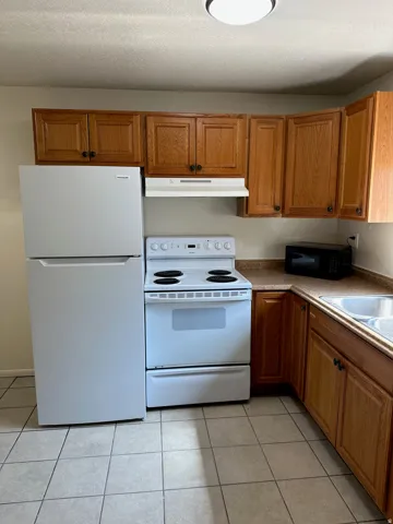 Kitchen featuring wood cabinetry, solid surface countertops, a stainless steel sink, and white appliances