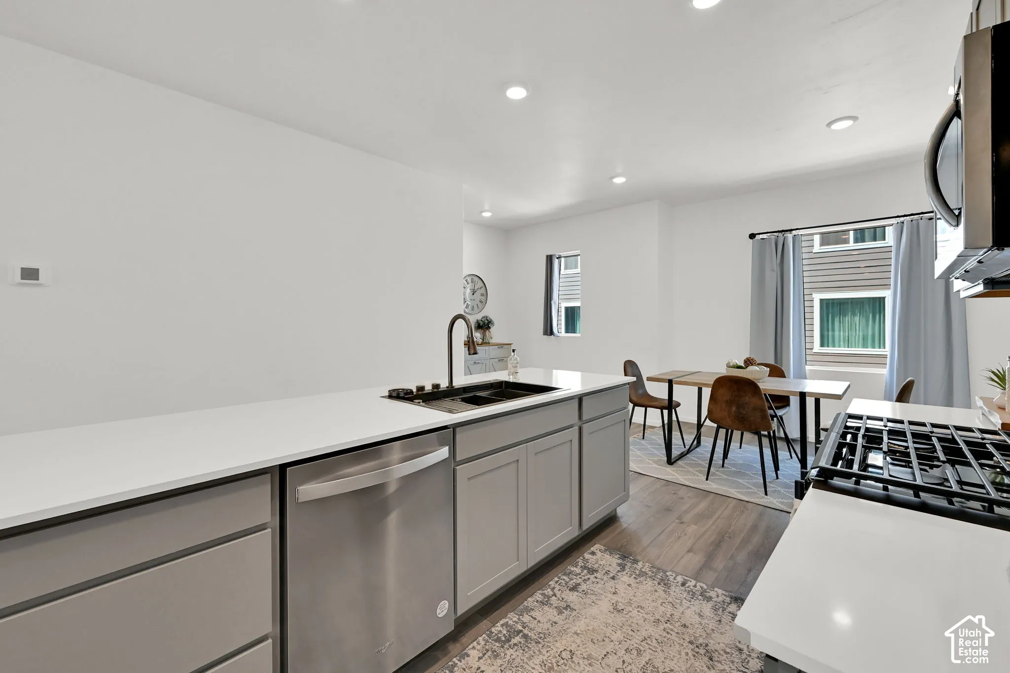 Modern kitchen featuring light gray cabinetry, stainless steel dishwasher, white countertops, and a black basin sink with a gooseneck faucet