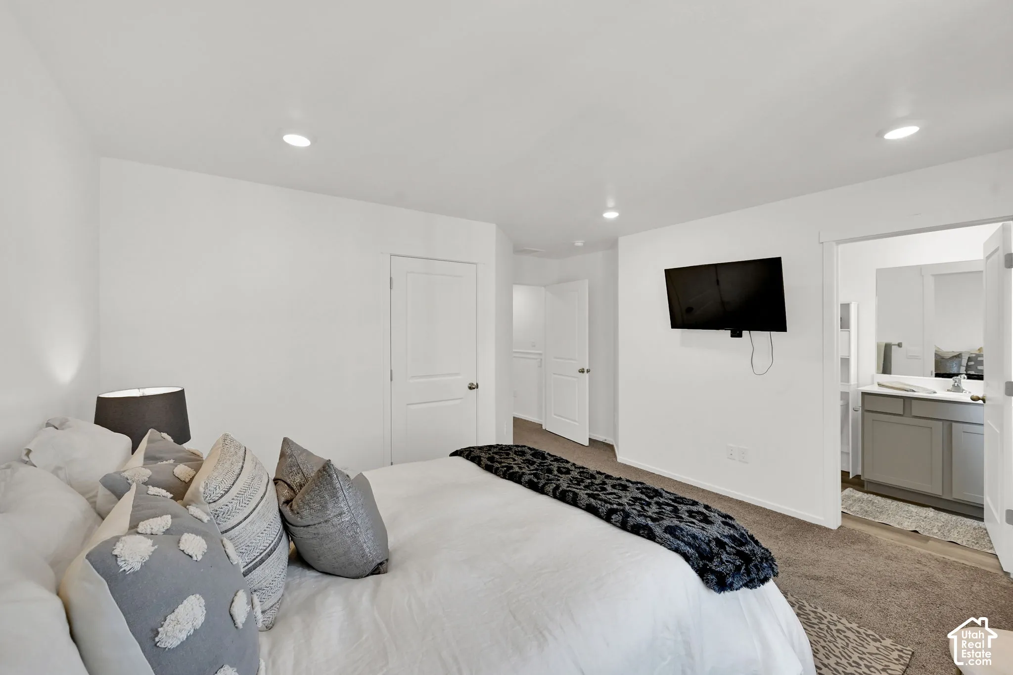Spacious bedroom with neutral-toned carpeting, recessed lighting, and a mounted display