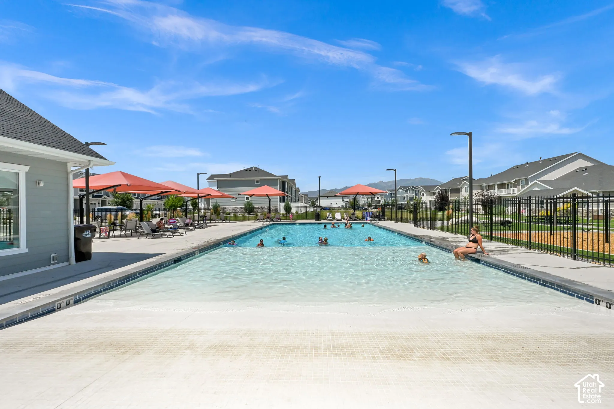 Resort-style pool area featuring an expansive swimming pool with a gradual entry, a surrounding concrete deck, and a clubhouse with light gray siding