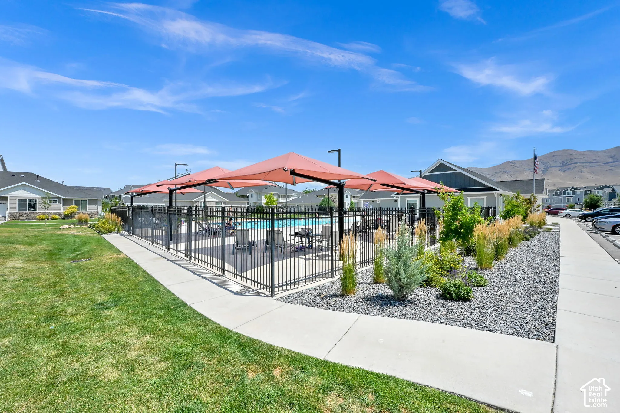 Community swimming pool featuring a black wrought iron fence, multiple large red umbrellas, and integrated lounge seating
