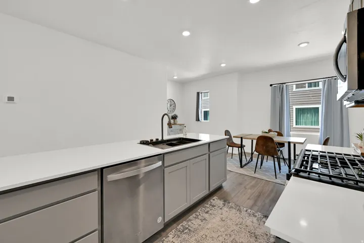 Modern kitchen featuring light gray cabinetry, stainless steel dishwasher, white countertops, and a black basin sink with a gooseneck faucet