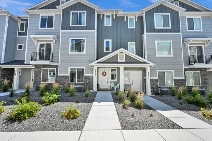Contemporary townhome with multi-level construction, featuring a stone facade accent, horizontal and vertical siding, a covered entry porch, and a second-story balcony with iron railing
