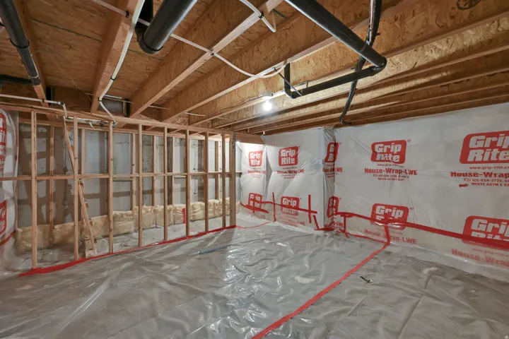 Unfinished basement with visible wood framing, exposed plumbing, and insulation