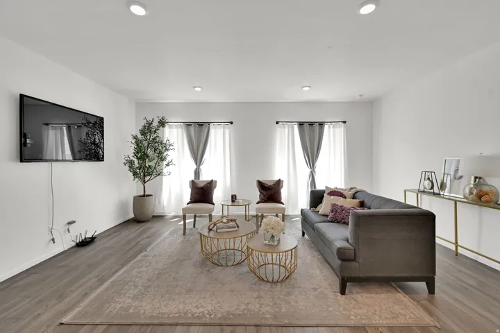 Living area featuring wood-finish flooring, recessed lighting, and dual windows with curtain rods