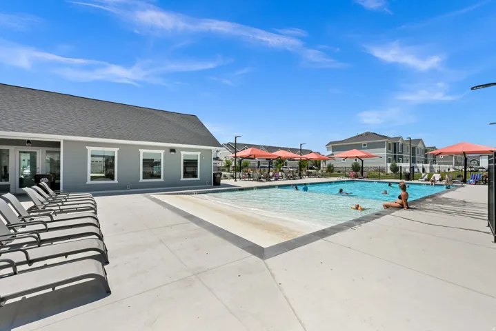 Outdoor swimming pool with an integrated sun ledge, surrounded by a concrete deck and a collection of lounge chairs