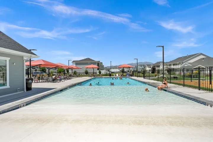 Resort-style pool area featuring an expansive swimming pool with a gradual entry, a surrounding concrete deck, and a clubhouse with light gray siding