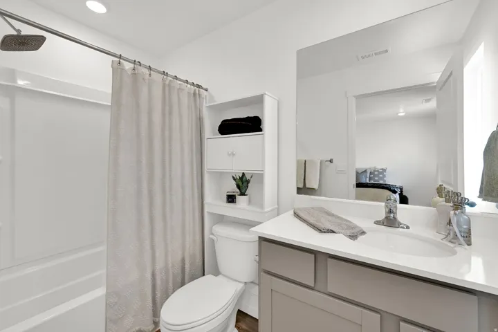 Bathroom featuring a full shower/tub combination with a square showerhead, a single vanity with a white countertop and integrated sink, and an expansive wall-mounted mirror
