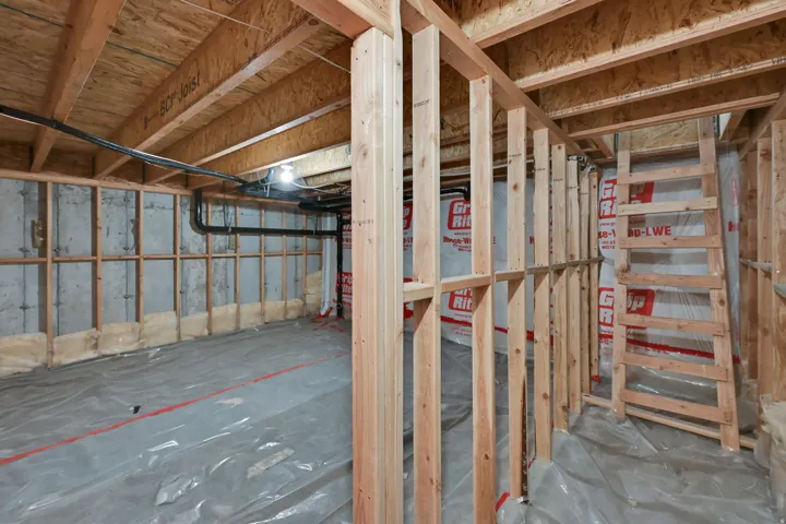 Unfinished basement space featuring exposed wood framing, concrete foundation walls, plumbing lines, and subfloor ceiling