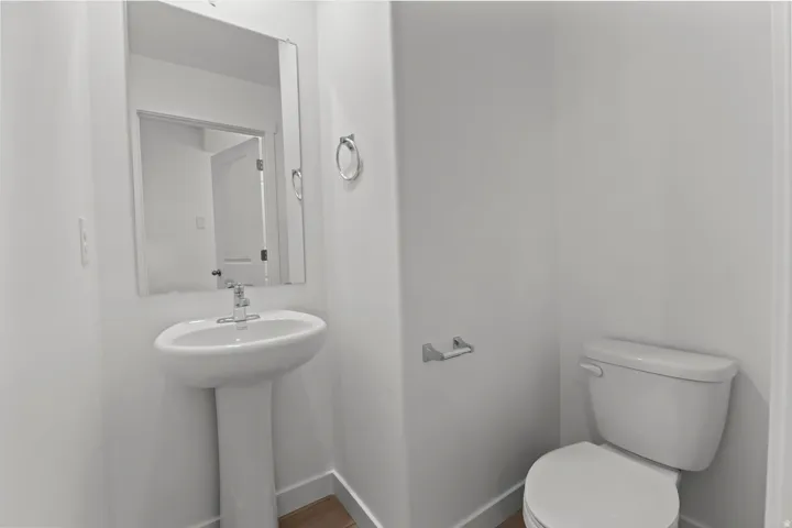Pedestal sink with chrome faucet and mirror, complemented by a white toilet and light wood-finish flooring
