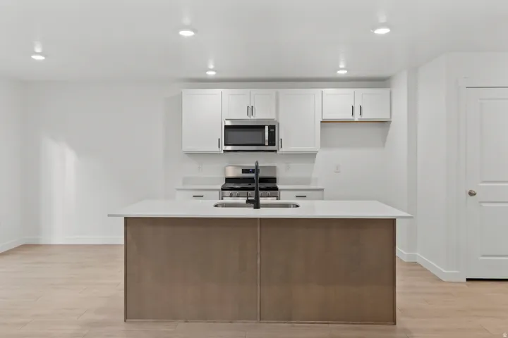 Kitchen featuring a central island with an undermount sink, light wood-finish flooring, white cabinetry with matte black hardware, stainless steel appliances, and recessed lighting