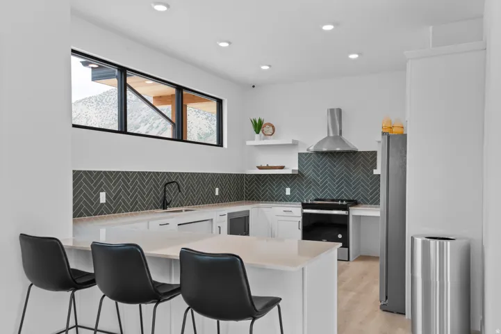 Contemporary kitchen featuring a herringbone tile backsplash, white cabinetry, integrated stainless steel appliances, a bar-height countertop, and a built-in kitchen island
