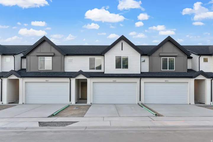 Contemporary townhouse facade featuring a two-tone exterior with white siding and gray paneling, dark shingle roofing, integrated garages with white doors, individual covered entryways, and concrete driveways